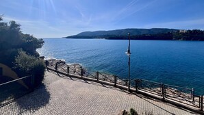 A paved waterfront promenade with a metal railing, overlooking a calm sea and distant hills. - La Pianotta suite with seaview (Porto Azzurro)