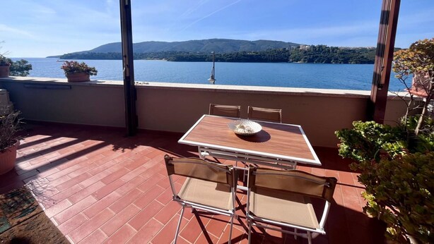 A terrace with a table and chairs, overlooking a lake with mountains in the background. - La Pianotta suite with seaview (Porto Azzurro)