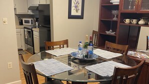 A dining area with a glass table surrounded by wooden chairs, a chandelier, and a kitchen in the background. - Charming 2-bedroom condo with fitness room and WiFi in fabulous Sugar Mountain (Sugar Mountain)