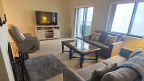 A living room with a sofa, armchair, coffee table, and a TV on a stand. - Charming 2-bedroom condo with fitness room and WiFi in fabulous Sugar Mountain (Sugar Mountain)
