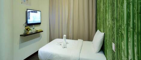 A hotel room with a bed, a television on a shelf, and a green curtain.