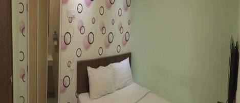 A hotel room with a bed, a wall-mounted air conditioner, and a patterned wallpaper.