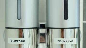 Two cylindrical dispensers labeled "SHAMPOOING" and "GEL DOUCHE" in a bathroom setting.