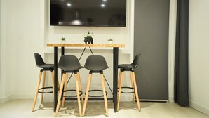 Une chambre moderne dotée d’un grand téléviseur à écran plat fixé au mur, d’une table en bois avec trois chaises noires et d’une petite plante en pot posée sur la table.