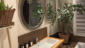 A bathroom with a wooden vanity, a white sink, a large mirror, and a potted plant. - Cosy village house (Peynier)