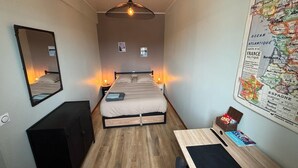 Hotellihuone, jossa on sänky, yöpöytälamput, seinällä oleva kartta, työpöytä tuolilla ja peili.