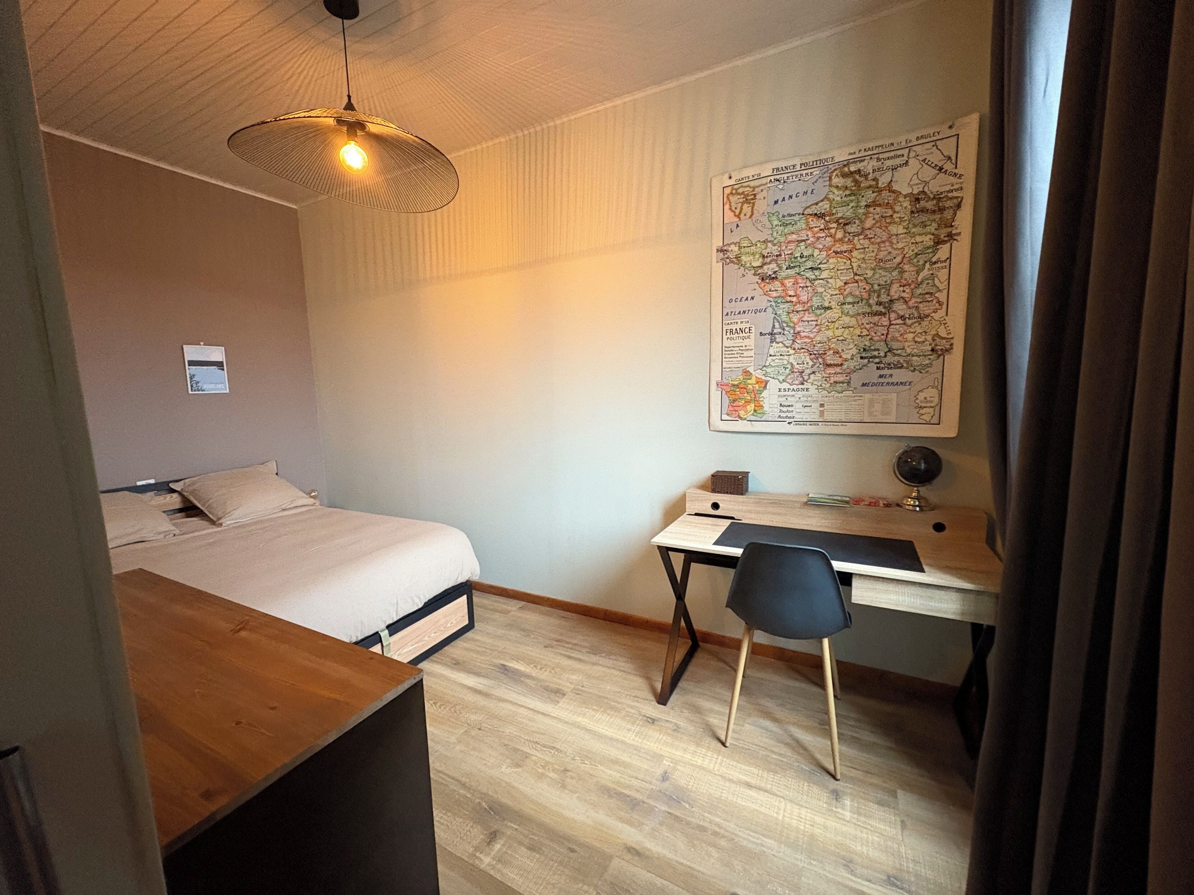 A bedroom with a bed, desk, chair, and a map on the wall.