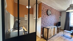 Moderni keittiö, jossa on kahvinkeitin, jääkaappi ja tiiliseinä, jossa on kello.