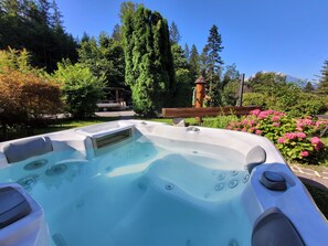 Een hottub in een tuin met een houten terras, omringd door bomen en bloemen.