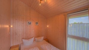 Une pièce en bois avec un lit, une fenêtre et un luminaire au plafond.