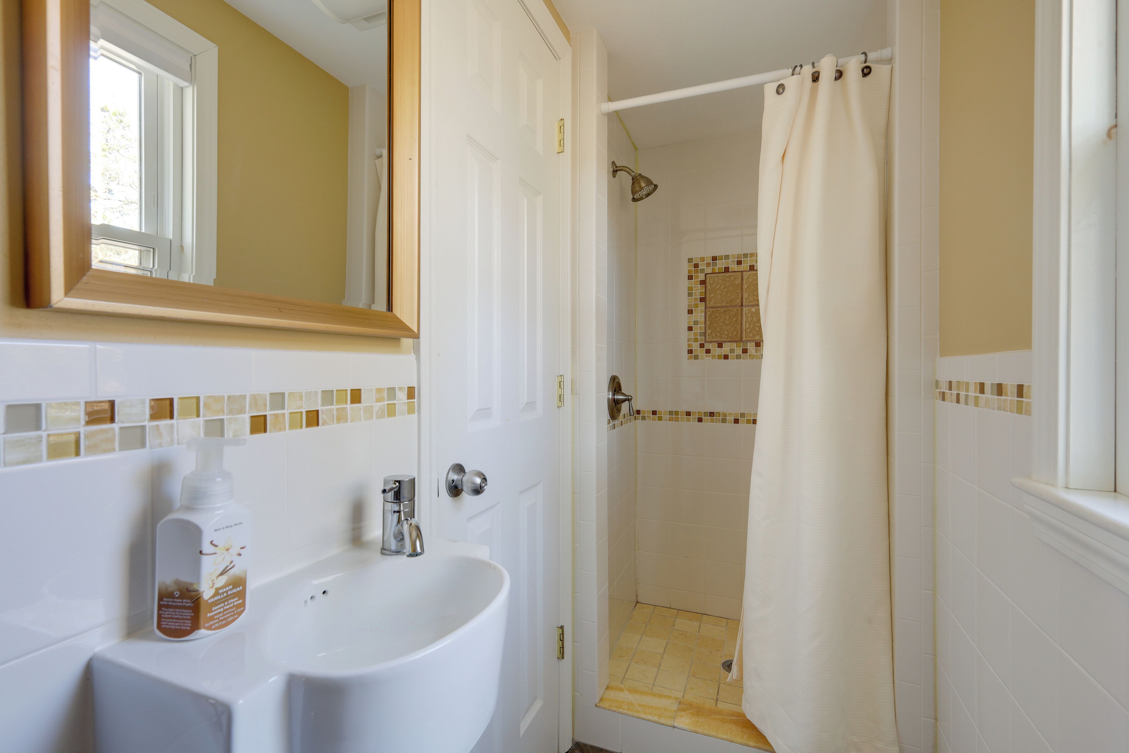 Un baño con lavamanos blanco, espejo y zona de ducha con cortina beige.