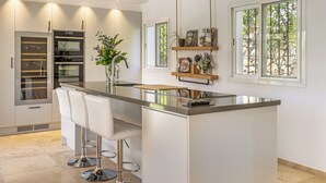 A modern kitchen with a central island, bar stools, and a built-in oven. - Villa Birkin by Vacation Marbella (Nueva Andalucía)