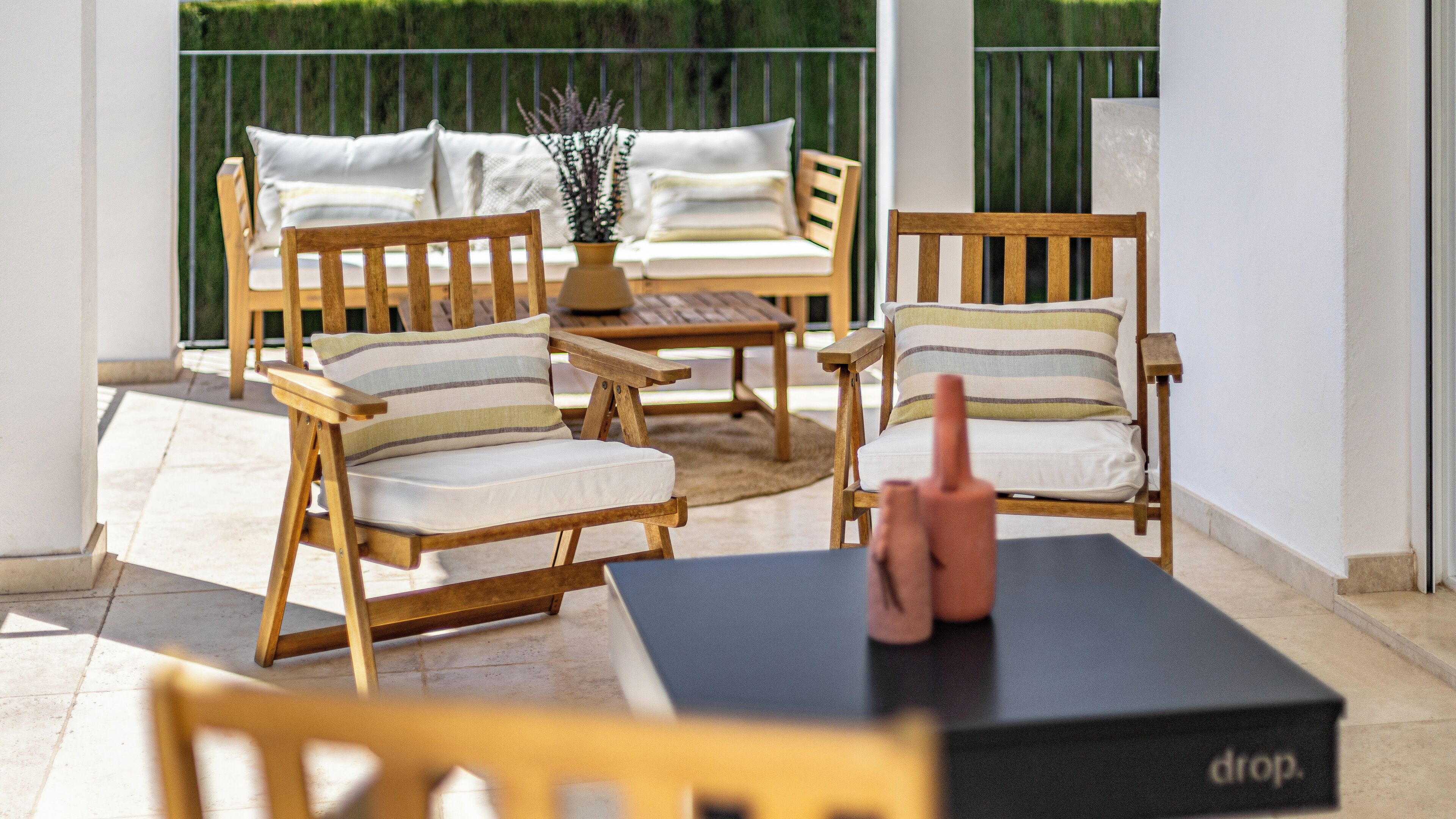 A patio area with wooden furniture including chairs and a sofa, a small table, and a black box with the word "drop" on it.