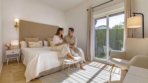 A modern bedroom with a large bed, a nightstand with a lamp, a sitting area with a chair, and a view of a balcony. - Villa Birkin by Vacation Marbella (Nueva Andalucía)