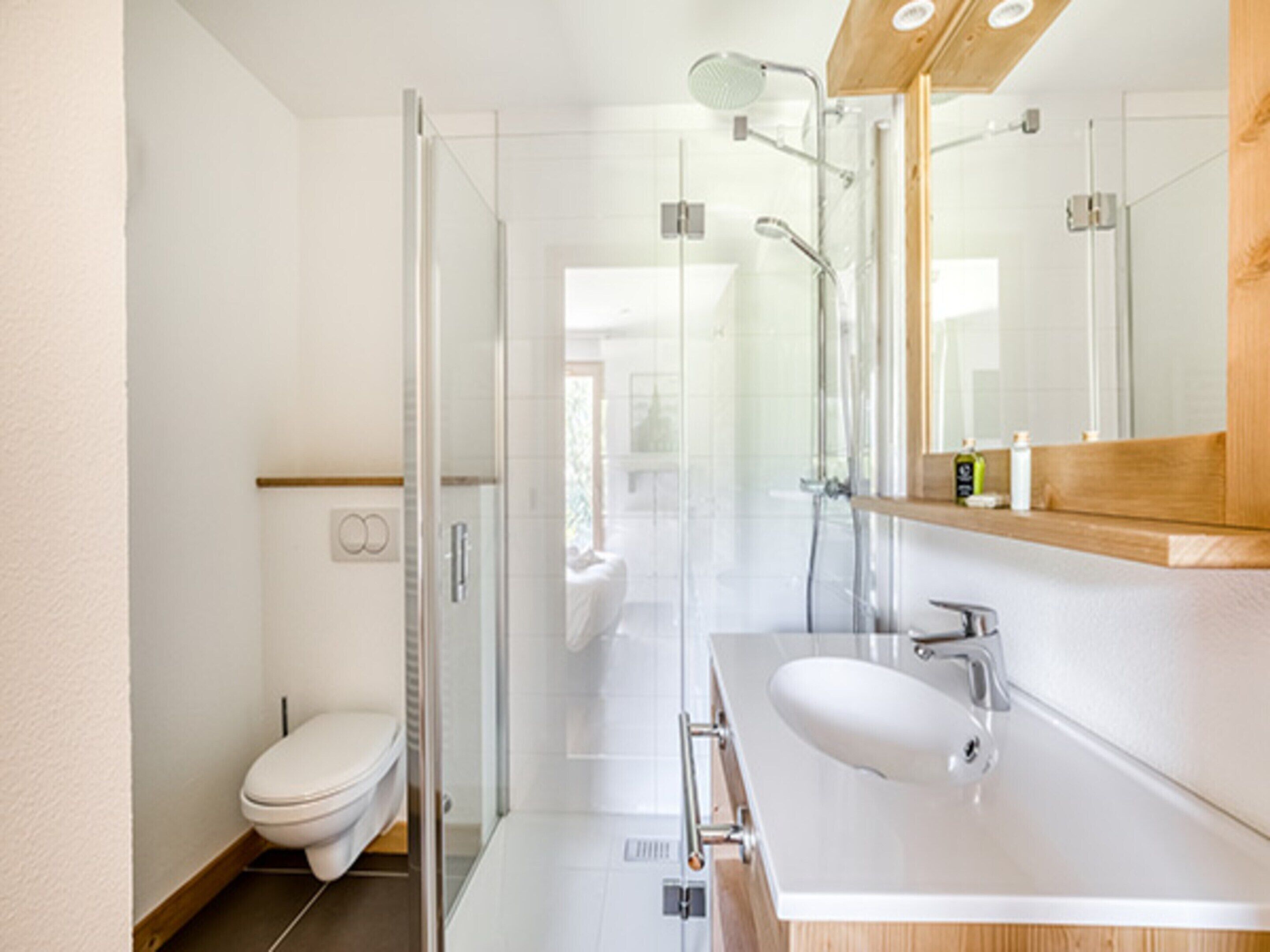A modern bathroom with a glass shower enclosure, a white toilet, and a vanity with a mirror and sink.