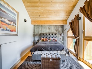 A bedroom with a large bed, a wooden ceiling, a window with curtains, and a painting on the wall. - Chalet in Combloux With Mont-blanc Views (Combloux)