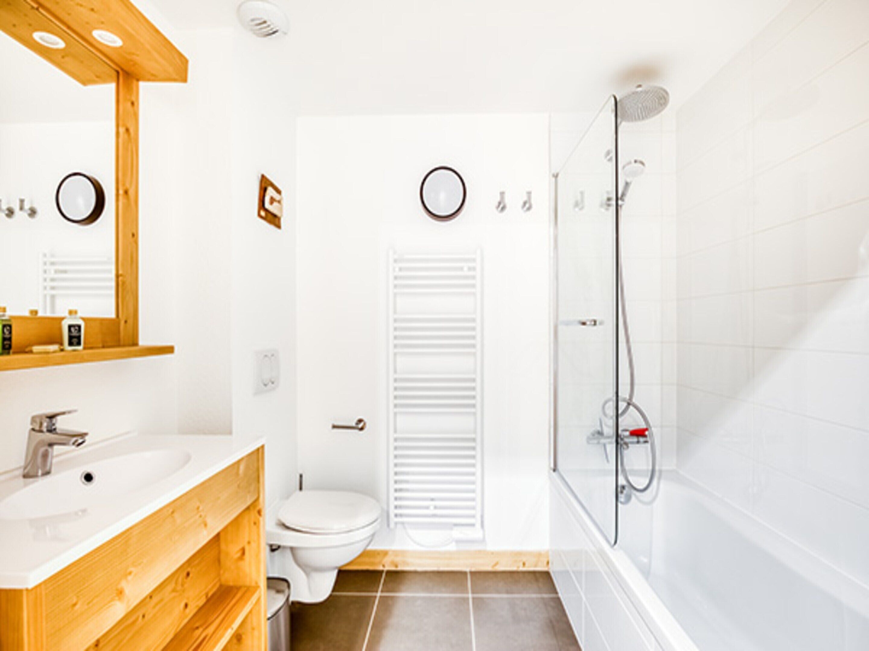 A modern bathroom with a wooden vanity, a toilet, a shower, and a mirror.