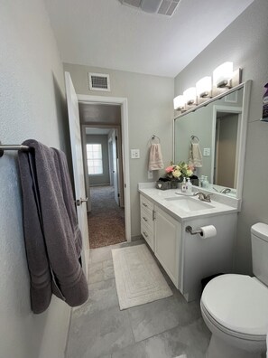 A bathroom with a white sink, mirror, and toilet. There are towels hanging on a rack and a rug on the floor.