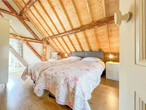 Una camera da letto con soffitto in legno, un letto con lenzuola a motivi floreali, un comodino e una sedia.