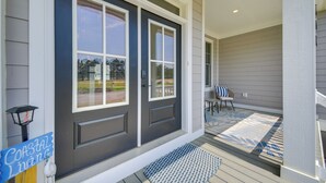 Una entrada de casa con una puerta gris oscura, un felpudo azul y un letrero que dice 'Coastal Living'.
