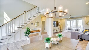 Un amplio espacio de sala con una mesa de comedor de madera, asientos cómodos, una escalera y una lámpara moderna.
