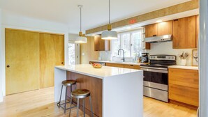 A modern kitchen with wooden cabinets, a large island with stools, stainless steel appliances, and a window providing natural light. - 2 Mi to Hoosic River: 'The Moss House' w/ Deck! (Eagle Bridge)