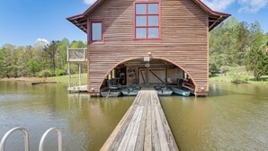 Une cabane en bois avec un quai s’avançant dans un lac, comprenant une zone abritée pour la mise à l’eau des bateaux et plusieurs embarcations.