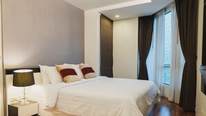 Una habitación de hotel moderna con una cama grande, una mesita de noche con lámpara y vistas al exterior a través de una ventana con cortinas.