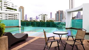 Una terraza en la azotea con barandilla de cristal, piscina y mesa con sillas.
