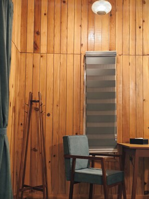 A room with wooden panel walls, a standing easel, a chair, a table, and a window with blinds. - Himkosi Farm by the River (Almora)