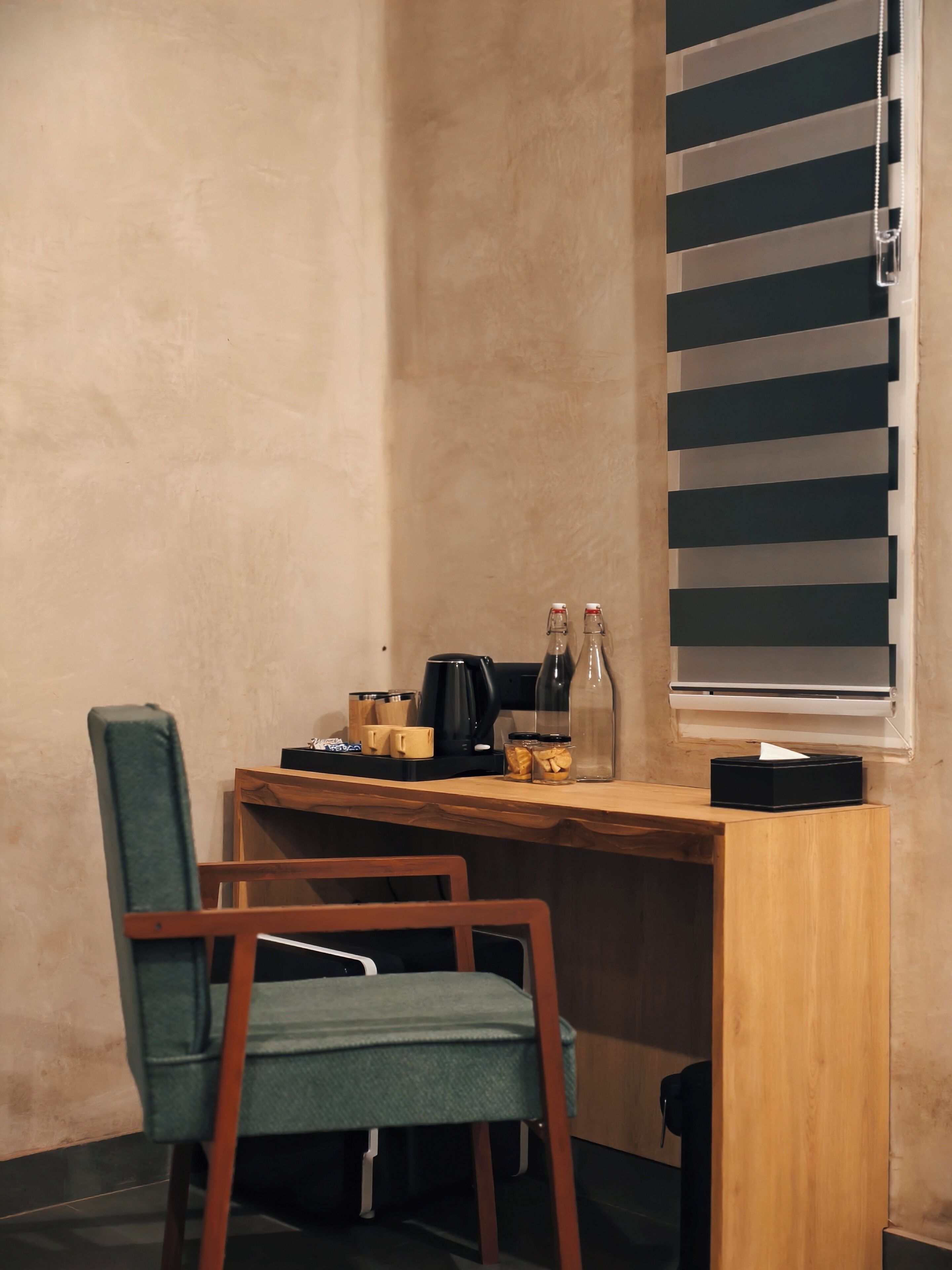 Un espacio de trabajo pequeño y acogedor con un escritorio de madera, una silla verde, una cafetera y una ventana con persianas.
