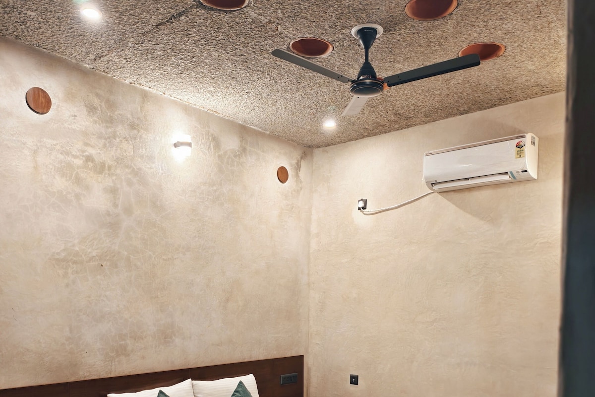 Un dormitorio con cama, mesita de noche, aire acondicionado en la pared y ventilador de techo.