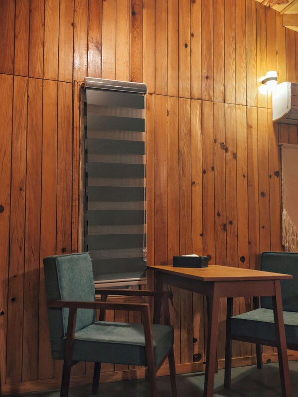 A room with wooden panel walls, a window with blinds, a table, and two chairs.