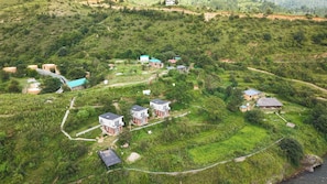 Zona rural con campos en terrazas, algunas casas y un edificio pequeño con techo azul.