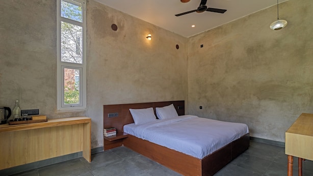 Ein Schlafzimmer mit einem hölzernen Bett, einem Nachttisch, einem Schreibtisch und einem Fenster mit Blick auf Bäume.