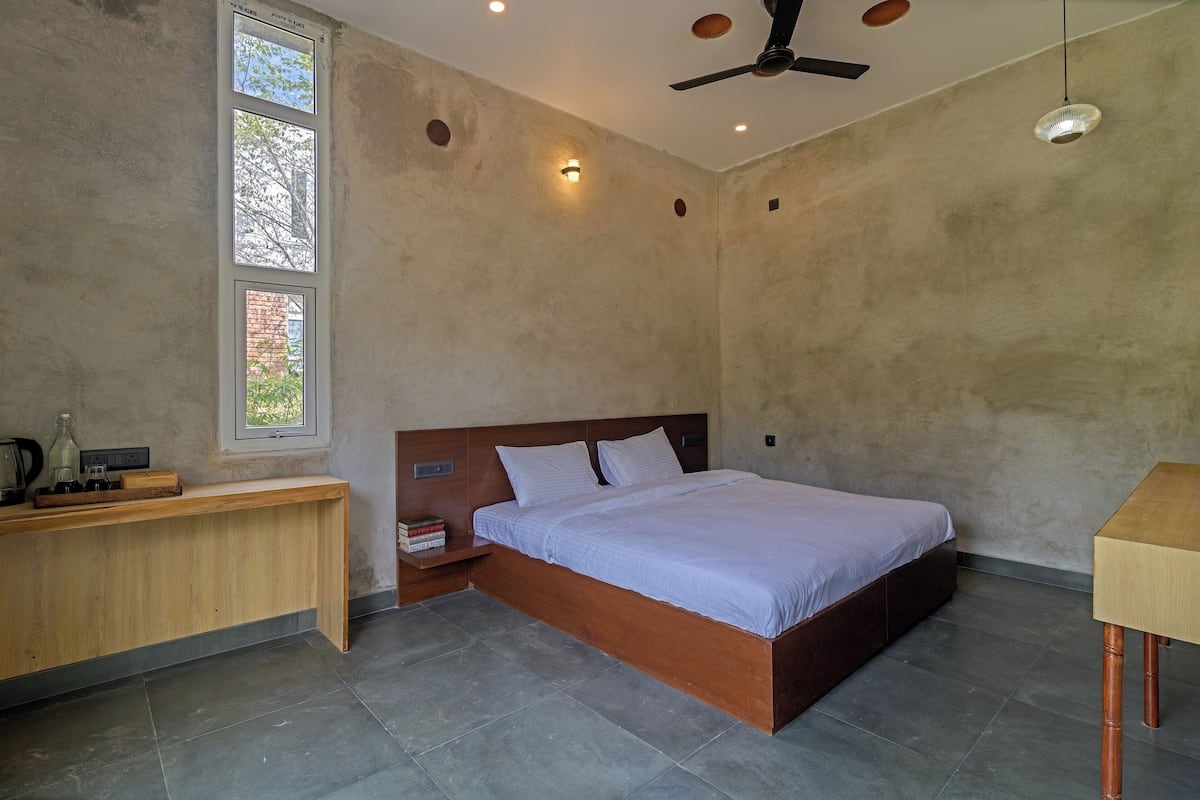 A bedroom with a wooden bed, a nightstand, a desk, and a window with a view of trees.