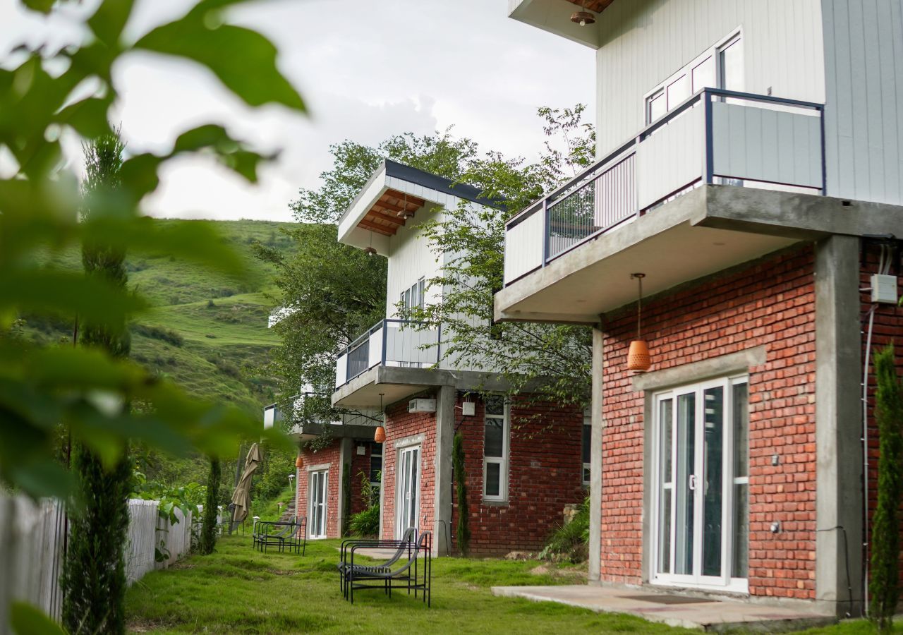 A modern building with a brick facade, a balcony, and a small garden area with a bench.