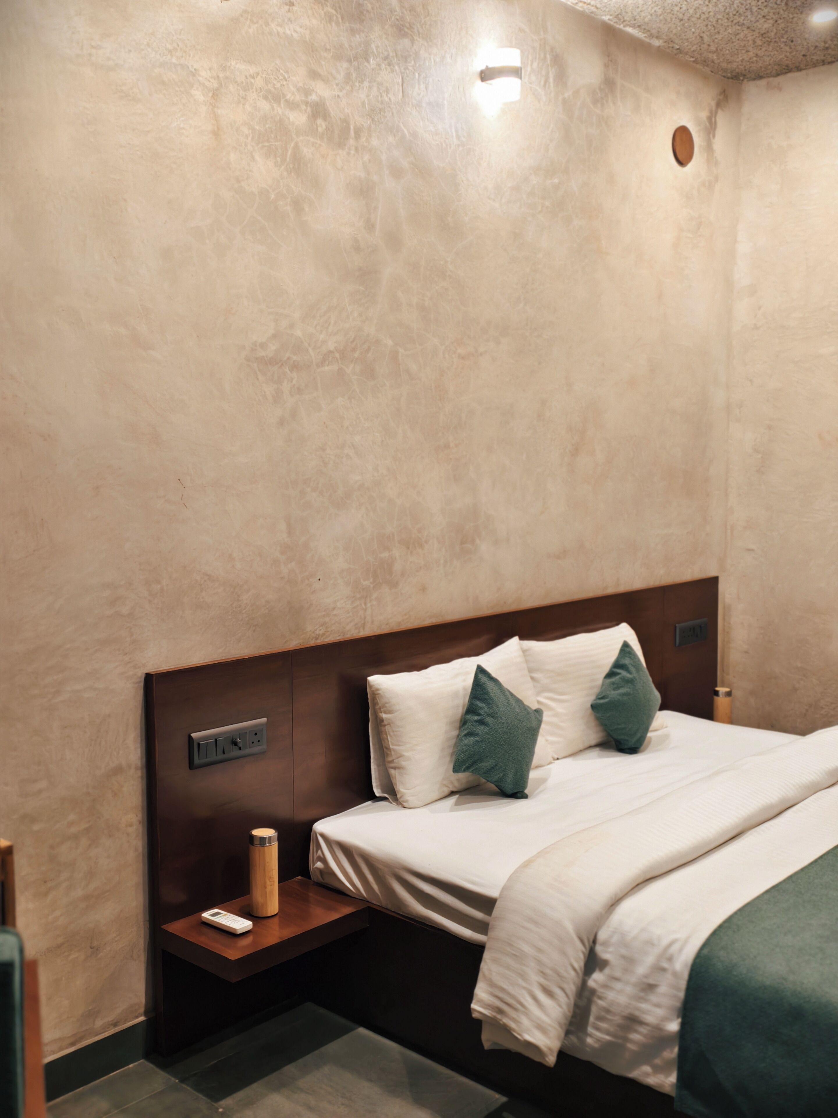Une chambre d’hôtel avec un lit, une table de chevet et un luminaire fixé au mur.