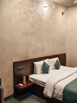 Une chambre d’hôtel avec un lit, une table de chevet et un luminaire fixé au mur.