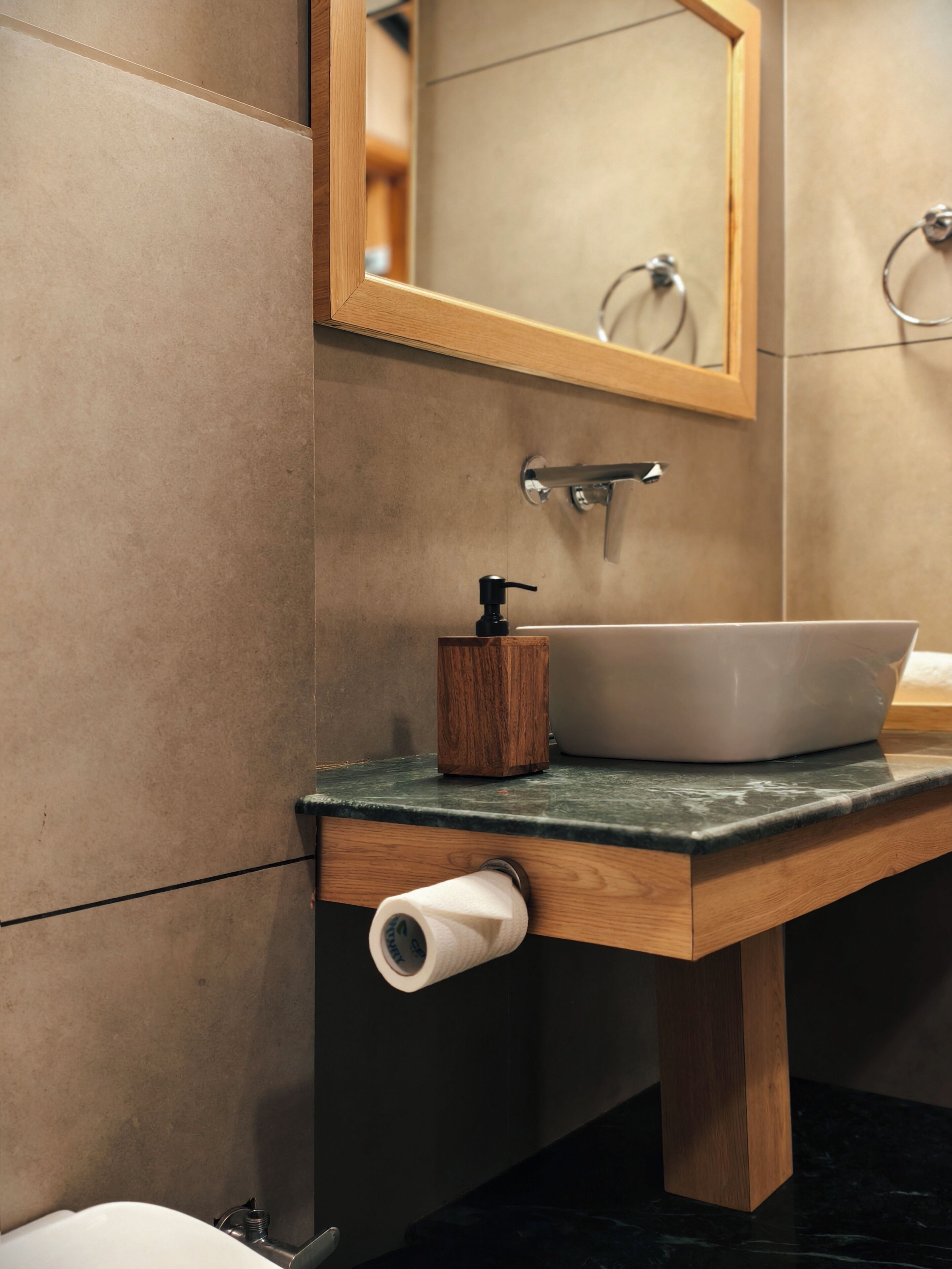 Un baño con tocador de madera, un lavamanos blanco, un espejo y un dispensador de papel higiénico.
