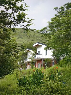 Un bâtiment à deux étages doté d’un balcon, entouré d’une végétation luxuriante et situé dans un paysage vallonné.