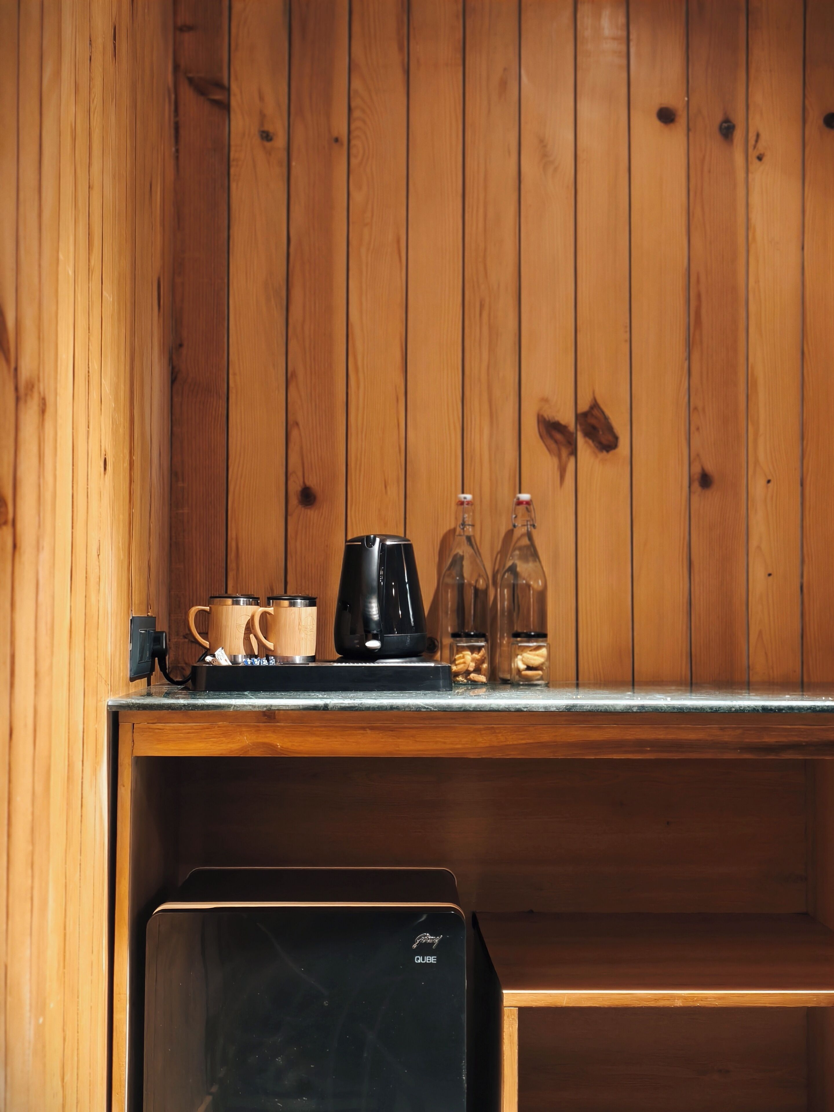 Un interior de madera con una encimera que sostiene una cafetera, tazas y botellas.