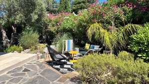 A garden with a stone pathway, a black metal chair, a small table, and various plants and flowers. - Villa Céleste, Apartment in villa, Swimming pool, garden, quiet, near the sea (Cavalaire-sur-Mer)
