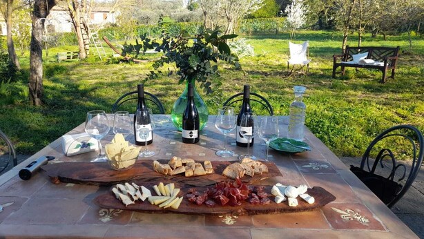 An outdoor dining setup with a table set for a meal, including a variety of cheeses, charcuterie, and wine bottles. - Merula. Organic winery farm between Orvieto and Lake Bolsena (orvieto)