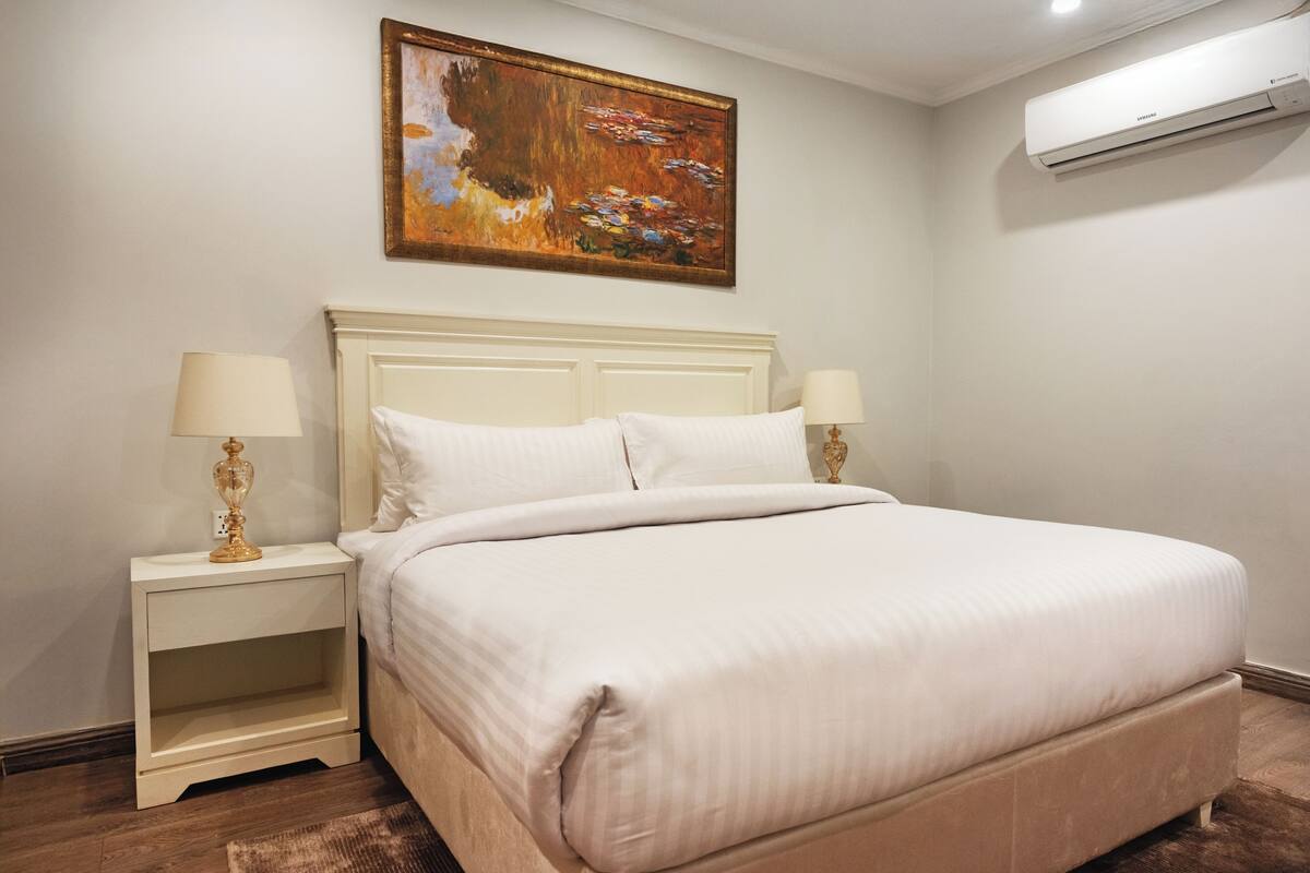 A neatly made bed with white linens, a white headboard, and two bedside tables with lamps.