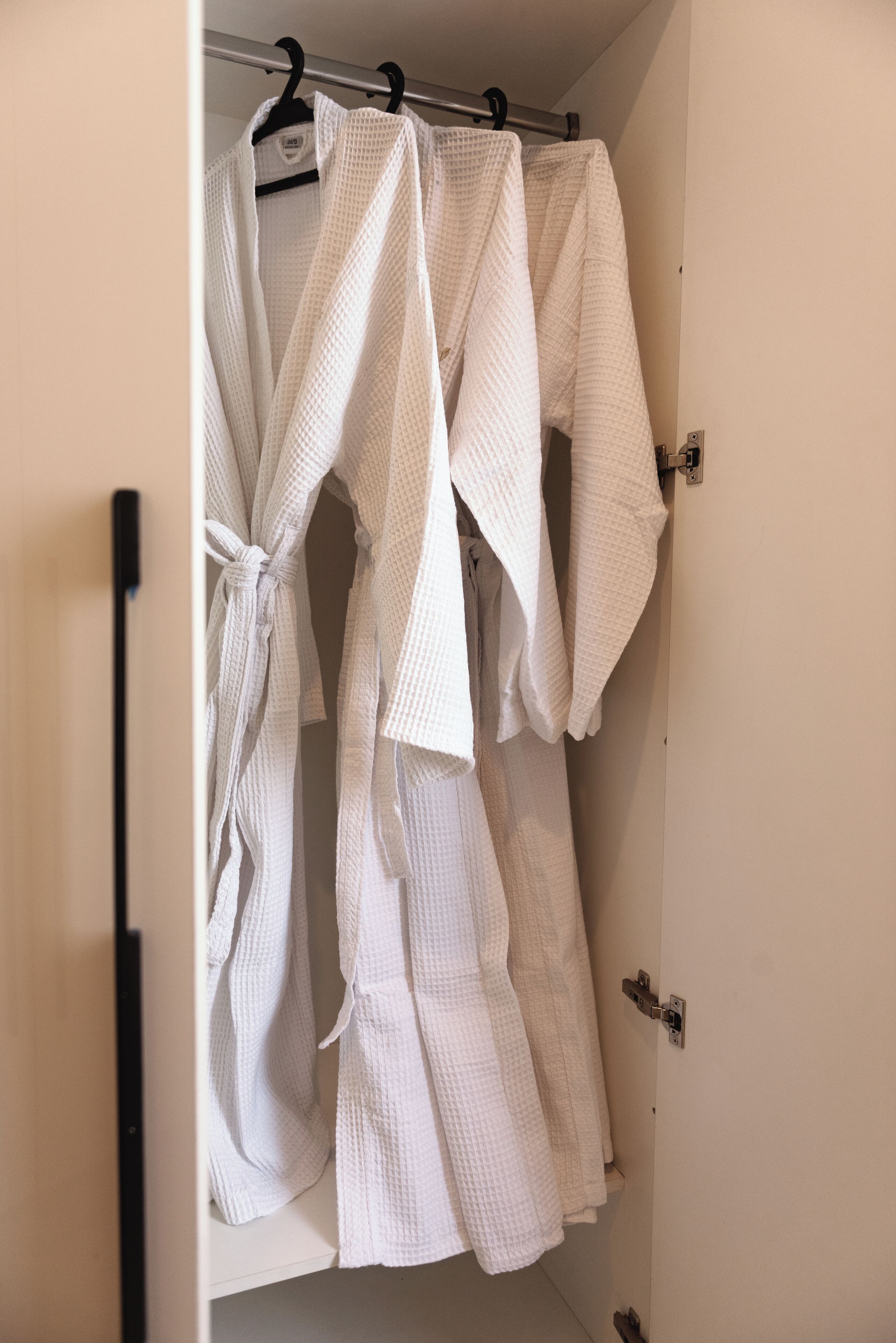 A closet with several white robes hanging on a rod.