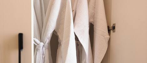 A closet with several white robes hanging on a rod.