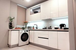 Uma cozinha moderna com armários brancos, máquina de lavar embutida e bancada com diversos eletrodomésticos e objetos decorativos.
