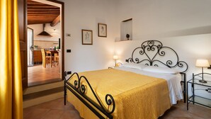 A bedroom with a bed, bedside lamps, a nightstand, a framed picture, and a view into the kitchen.