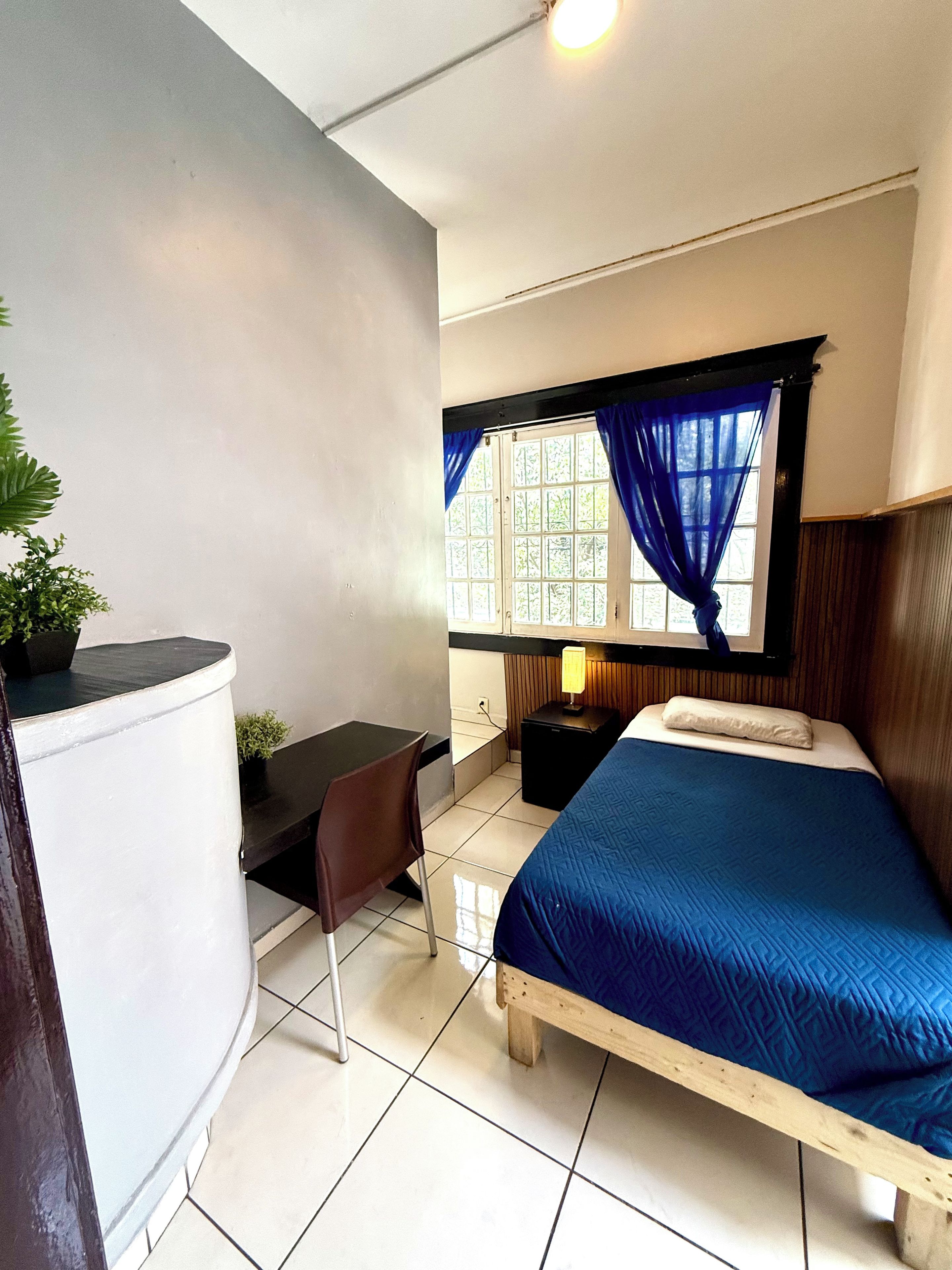 A room with a bed, a desk, a chair, a lamp, and a window with curtains.